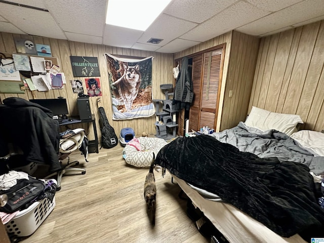 bedroom with a paneled ceiling, wooden walls, visible vents, and wood finished floors