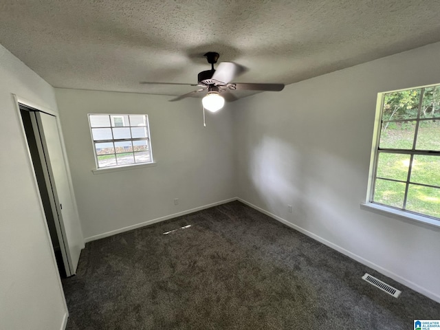 unfurnished bedroom with baseboards, multiple windows, visible vents, and dark colored carpet
