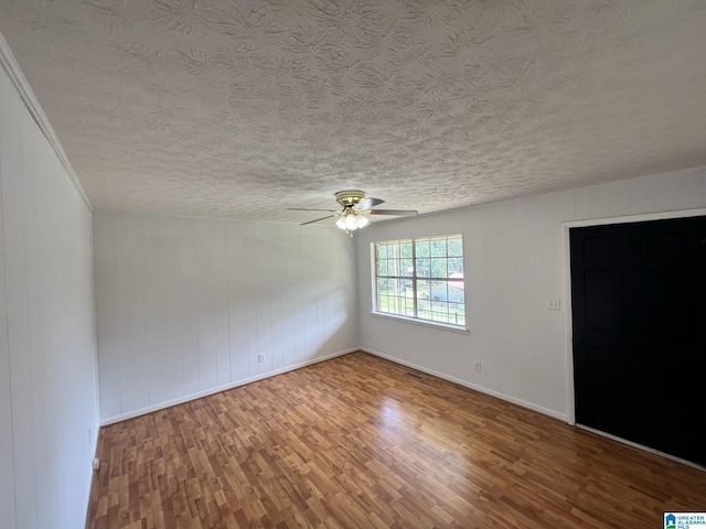 empty room featuring ceiling fan, a textured ceiling, wood finished floors, visible vents, and baseboards