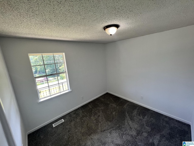 spare room featuring visible vents, dark carpet, a textured ceiling, and baseboards