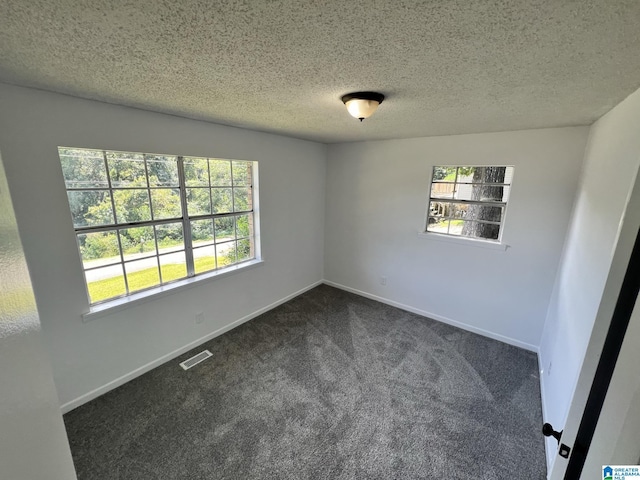 empty room with dark colored carpet, plenty of natural light, visible vents, and baseboards
