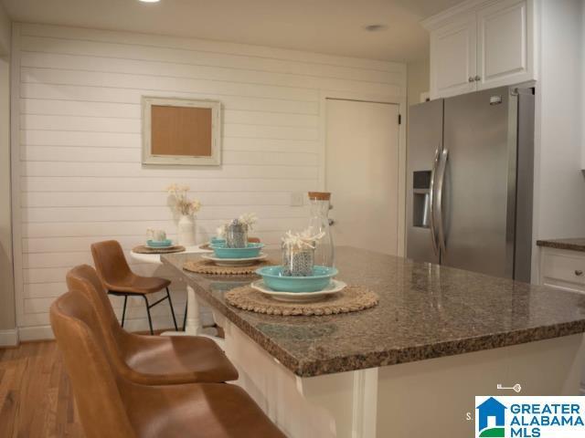 kitchen with stainless steel refrigerator with ice dispenser, light wood finished floors, white cabinets, dark stone countertops, and a kitchen bar