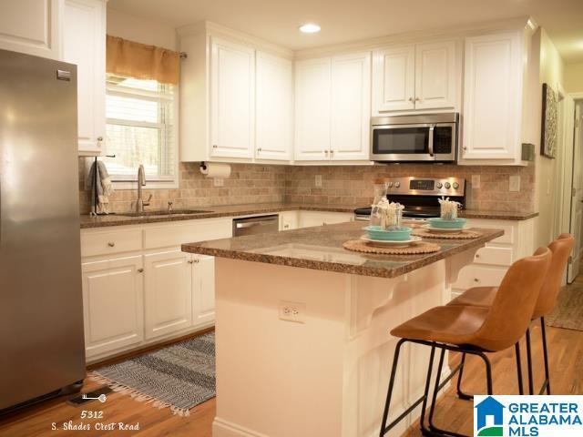 kitchen featuring dark stone counters, appliances with stainless steel finishes, wood finished floors, white cabinetry, and a sink