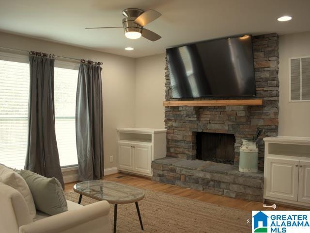 living area with light wood-style flooring, a fireplace, visible vents, and ceiling fan