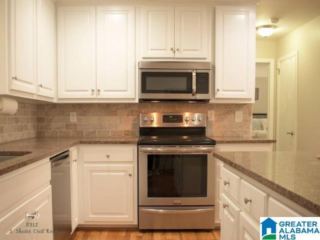 kitchen with stone counters, white cabinetry, light wood-style floors, appliances with stainless steel finishes, and backsplash