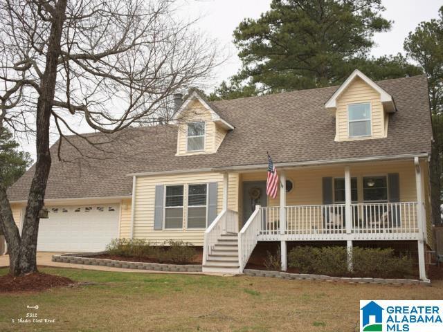 new england style home with an attached garage, a porch, roof with shingles, and a front yard