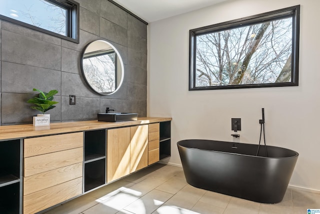 bathroom featuring baseboards, a soaking tub, tile patterned flooring, vanity, and tile walls