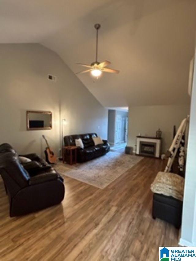 living area with high vaulted ceiling, a fireplace, a ceiling fan, and wood finished floors