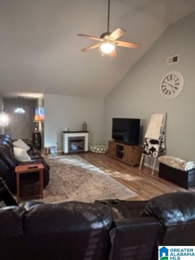 living area featuring a fireplace, visible vents, a ceiling fan, wood finished floors, and high vaulted ceiling