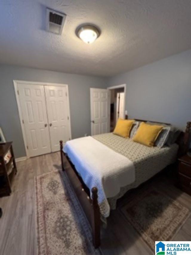 bedroom featuring a closet, visible vents, a textured ceiling, wood finished floors, and baseboards