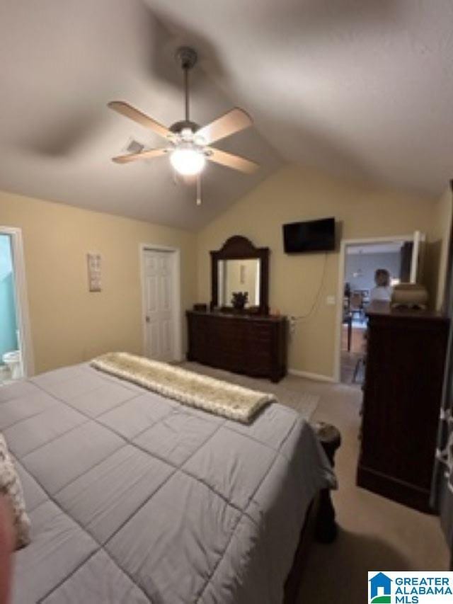 bedroom with vaulted ceiling, light carpet, connected bathroom, and a ceiling fan