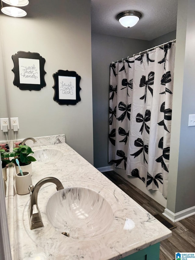 full bathroom featuring double vanity, a sink, a textured ceiling, and wood finished floors