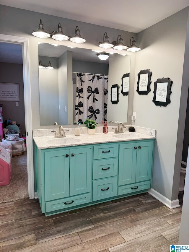 bathroom with double vanity, baseboards, a sink, and wood finished floors