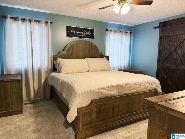 bedroom with a barn door, ceiling fan, a textured ceiling, and light colored carpet