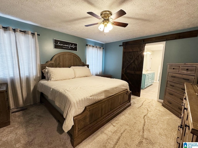 bedroom with visible vents, light colored carpet, a barn door, ceiling fan, and a textured ceiling