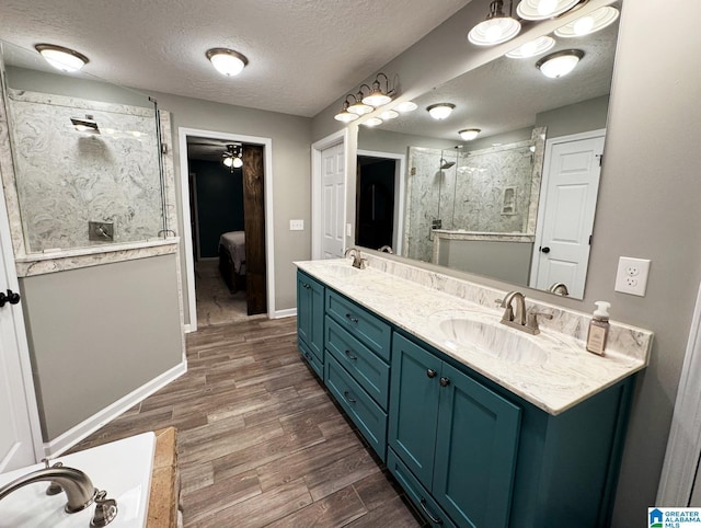 ensuite bathroom with a stall shower, double vanity, a sink, and wood finished floors