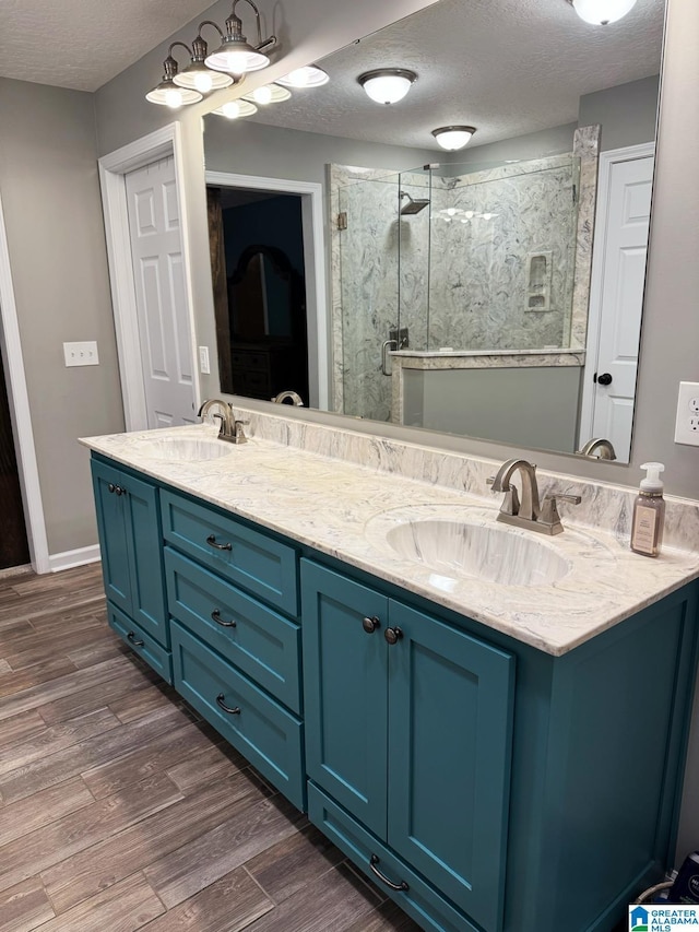 full bathroom featuring a stall shower, a sink, a textured ceiling, and wood finished floors