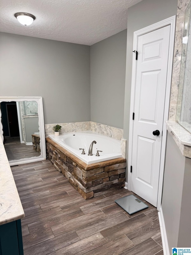 bathroom featuring a textured ceiling, vanity, a bath, and wood finish floors