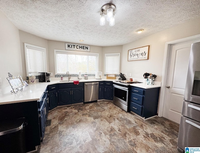 kitchen featuring blue cabinetry, light countertops, appliances with stainless steel finishes, a sink, and a textured ceiling