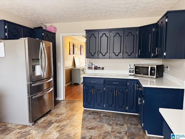 kitchen featuring blue cabinetry, light countertops, appliances with stainless steel finishes, stone finish flooring, and a textured ceiling