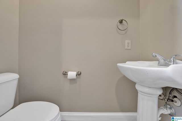 half bathroom featuring toilet, baseboards, and a sink