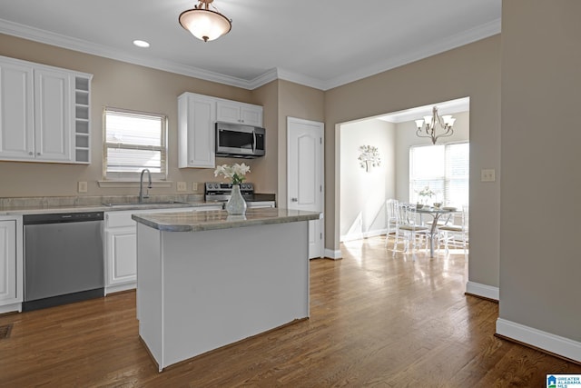 kitchen with stainless steel appliances, hanging light fixtures, white cabinetry, a sink, and a kitchen island