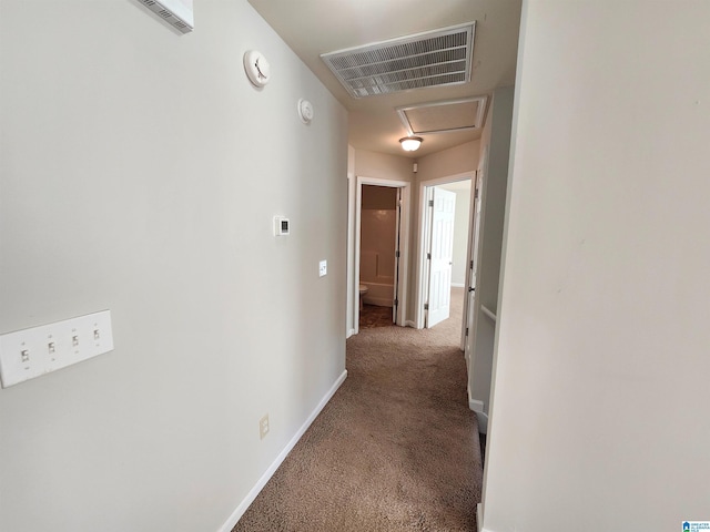 hallway with carpet floors, attic access, visible vents, and baseboards