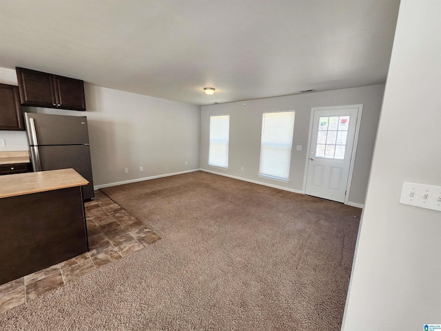 kitchen featuring open floor plan, light countertops, dark brown cabinets, freestanding refrigerator, and dark colored carpet