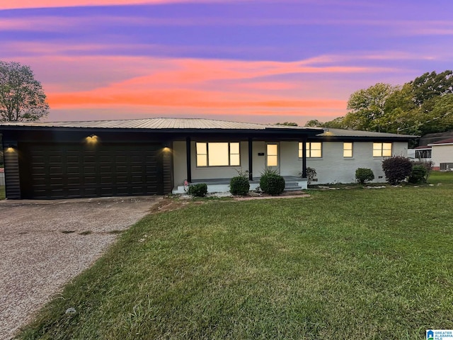 view of front facade featuring an attached garage, driveway, metal roof, and a front yard