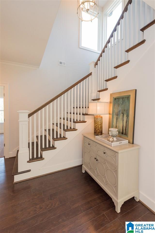 staircase featuring baseboards, visible vents, wood finished floors, crown molding, and a chandelier