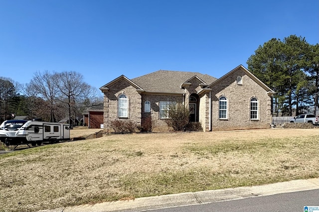 french provincial home featuring a shingled roof, brick siding, and a front lawn