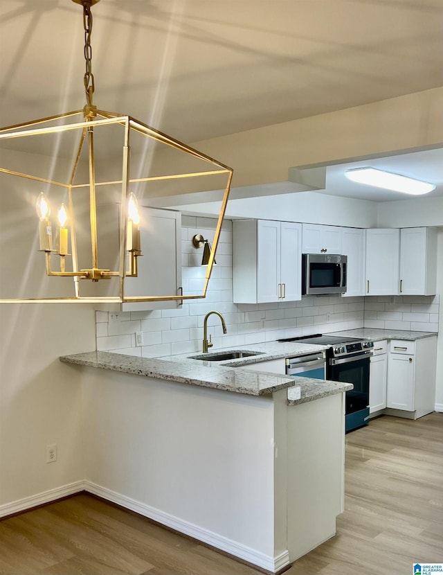 kitchen featuring backsplash, appliances with stainless steel finishes, a sink, light stone countertops, and light wood-type flooring