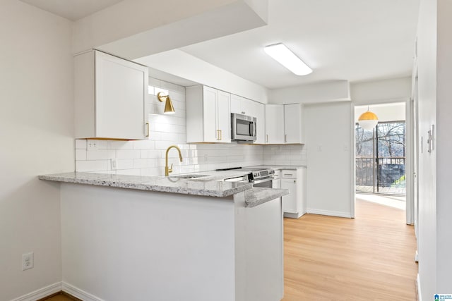 kitchen with light wood-style flooring, a sink, appliances with stainless steel finishes, backsplash, and light stone countertops