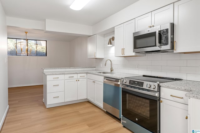 kitchen featuring tasteful backsplash, appliances with stainless steel finishes, a peninsula, white cabinetry, and a sink