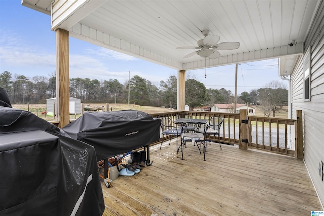 wooden terrace with outdoor dining space, ceiling fan, a storage unit, and an outbuilding