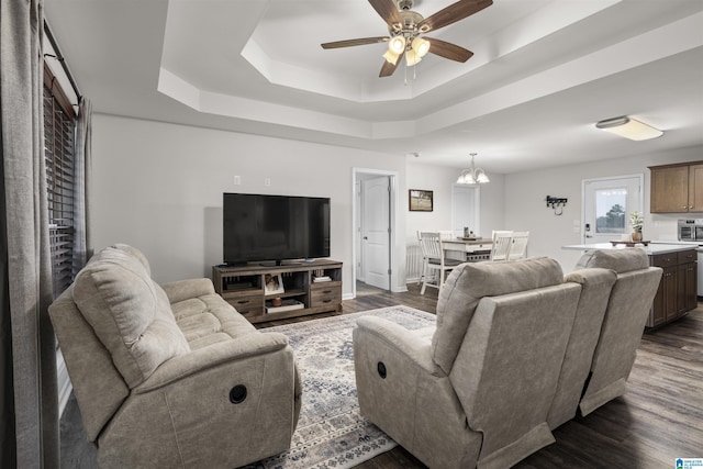 living room with ceiling fan with notable chandelier, a raised ceiling, and dark wood finished floors