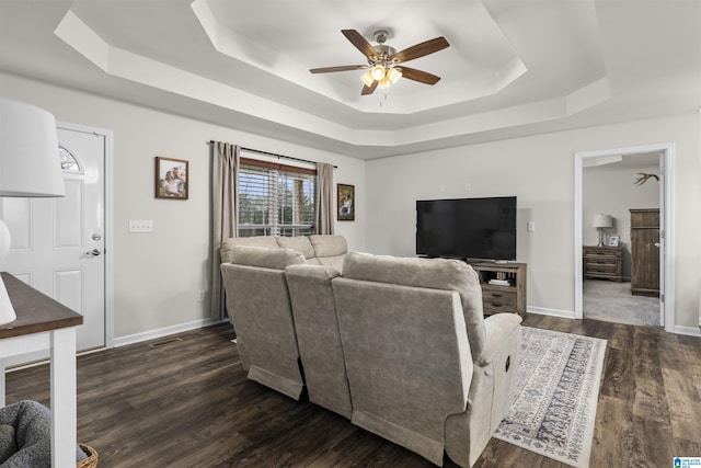 living room featuring dark wood-style floors, baseboards, a tray ceiling, and a ceiling fan