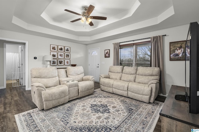 living area featuring ceiling fan, baseboards, a raised ceiling, and wood finished floors