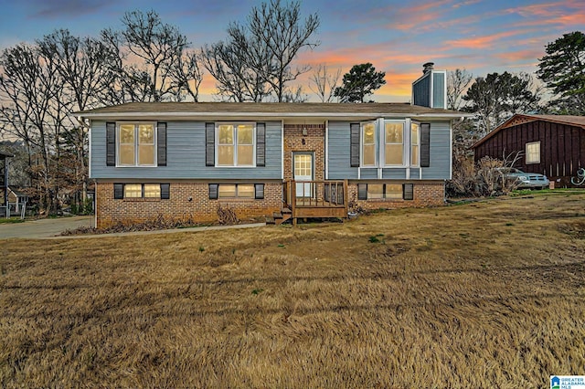 raised ranch with brick siding, a chimney, and a lawn