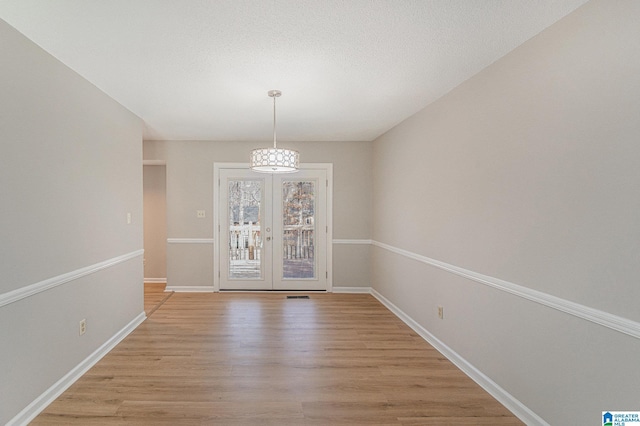 unfurnished dining area with french doors, light wood-style flooring, baseboards, and a textured ceiling