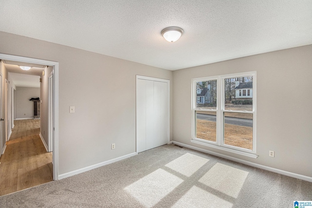 unfurnished bedroom featuring carpet, a closet, visible vents, a textured ceiling, and baseboards