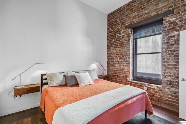 bedroom featuring baseboards, dark wood finished floors, and brick wall