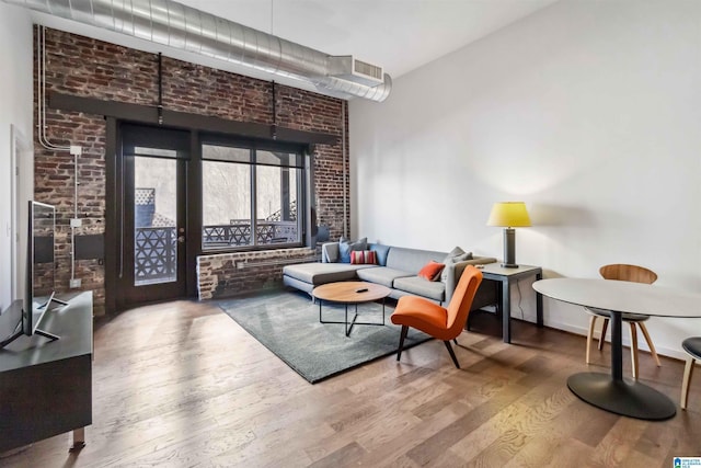 living area with brick wall, wood finished floors, and baseboards