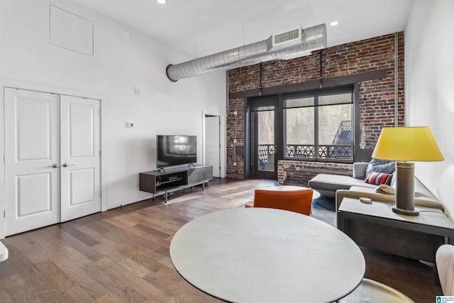 living room featuring a towering ceiling, brick wall, visible vents, and wood finished floors