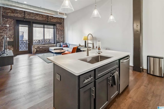 kitchen featuring pendant lighting, a center island with sink, light countertops, a sink, and dishwasher