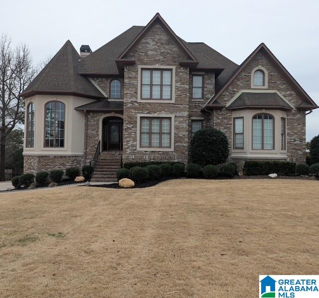 view of front of home featuring roof with shingles, a front lawn, a chimney, and brick siding