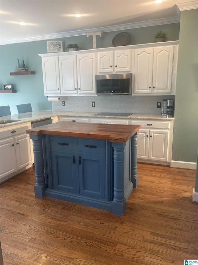 kitchen with wooden counters, black electric stovetop, stainless steel microwave, and white cabinets