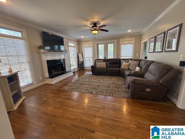 living room with crown molding, a fireplace with raised hearth, wood finished floors, and french doors