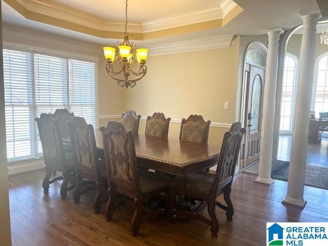 dining space with a tray ceiling, wood finished floors, decorative columns, and a notable chandelier