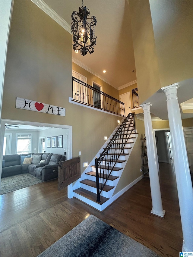 stairs featuring a towering ceiling, decorative columns, crown molding, and wood finished floors